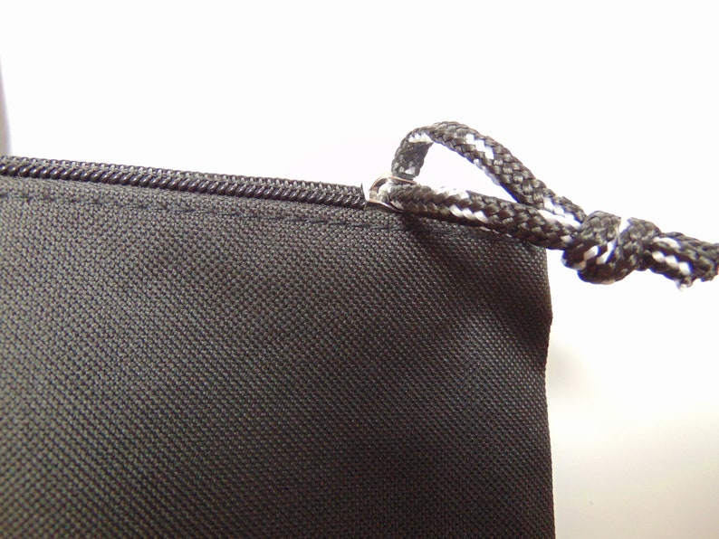Peut inclure: Gros plan d'un sac &agrave; cordon noir avec une fermeture &eacute;clair et un cordon blanc et noir. Le sac est fait d'un tissu r&eacute;sistant.