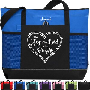 May include: A blue and black tote bag with a white heart design and the text "The Joy of the Lord is my Strength". The bag has a mesh pocket on the side and a zippered pocket on the front. The name "Hannah" is embroidered on the front pocket.