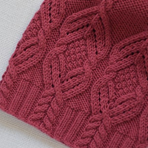 May include: Close-up of a deep red knitted fabric with a cable knit pattern.