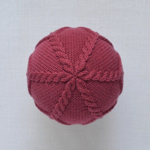 May include: A close-up of a knitted burgundy beanie with a cable knit pattern.
