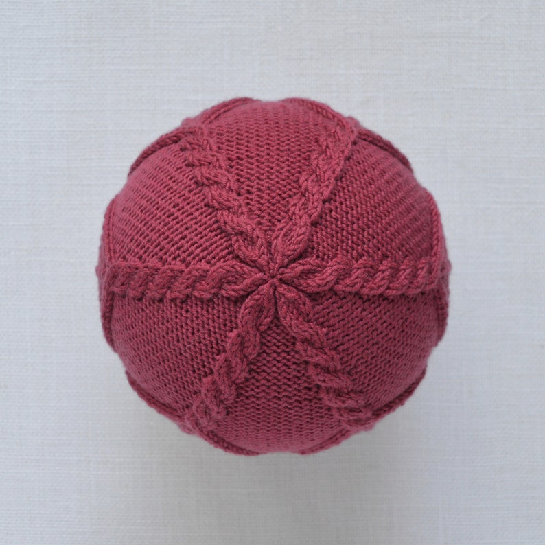 May include: A close-up of a knitted burgundy beanie with a cable knit pattern.