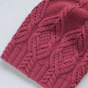May include: A pink knitted beanie with a cable knit pattern.