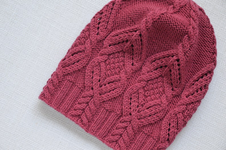 May include: A pink knitted beanie with a cable knit pattern.