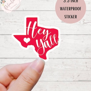 Puede incluir: Una pegatina impermeable de 8,9 cm que presenta un contorno rojo del estado de Texas con las palabras "Hey Y'all" en letra cursiva blanca y un corazón blanco.