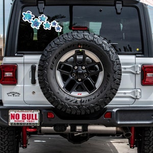 Puede incluir: Un Jeep Wrangler blanco con una rueda de repuesto negra y una matr&iacute;cula que dice "NO BULL SINCE 1951 EARNHARDT". Hay una pegatina de tortuga azul y verde en la ventana trasera.