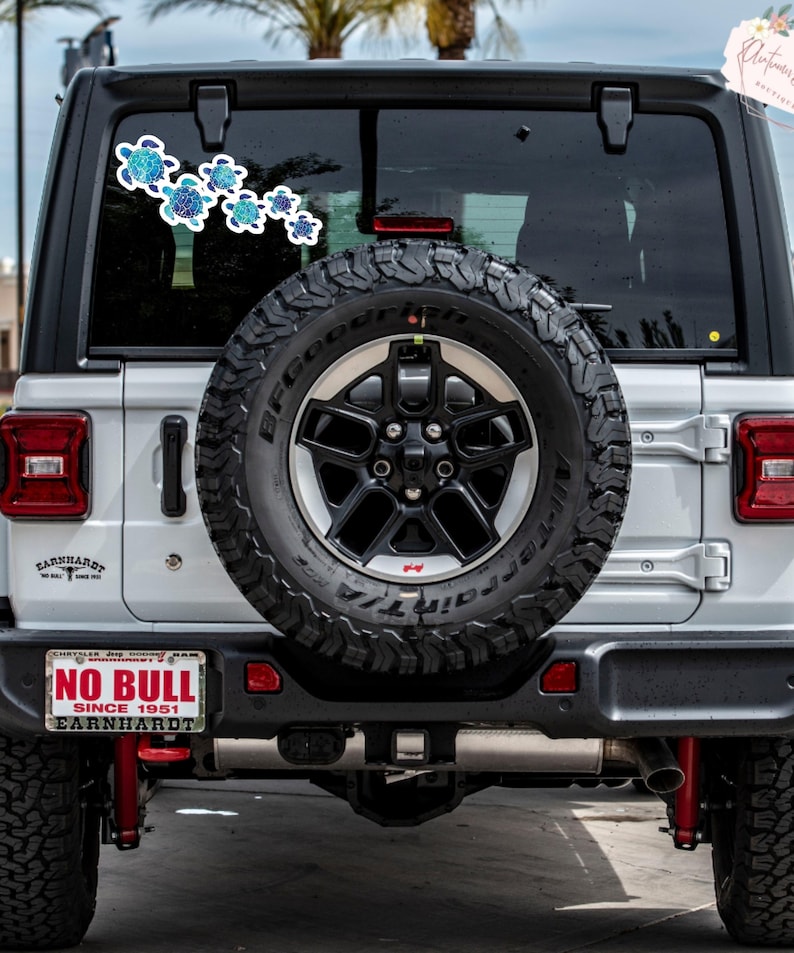 Puede incluir: Un Jeep Wrangler blanco con una rueda de repuesto negra y una matr&iacute;cula que dice "NO BULL SINCE 1951 EARNHARDT". Hay una pegatina de tortuga azul y verde en la ventana trasera.