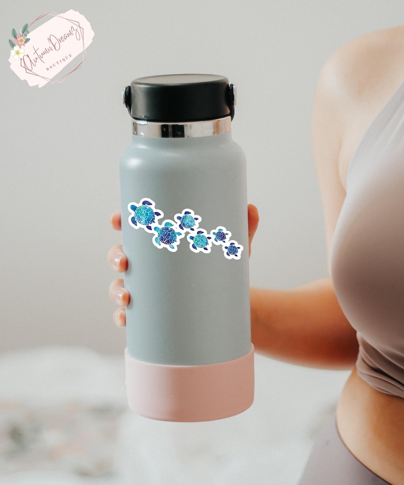 Puede incluir: Una botella de agua reutilizable gris con fondo rosa y una pegatina de un grupo de tortugas marinas azules y verdes nadando en l&iacute;nea.