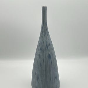 May include: A tall, blue and white striped ceramic vase. The vase has a conical shape that tapers to a narrow neck and a small opening at the top. The surface is decorated with vertical stripes.