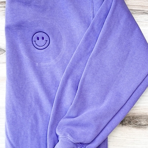 May include: A purple sweatshirt with a small embroidered smiley face on the front.