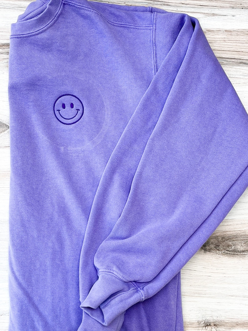May include: A purple sweatshirt with a small embroidered smiley face on the front.