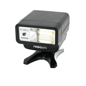 Pode incluir: Flash automático Nissin 400 HA preto para câmeras. O flash tem uma cabeça retangular com as palavras "AUTOMATIC" e "400 HA" impressas na frente. É montado em um suporte preto.