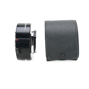 May include: A black Quantaray lens adapter with a red dot and a black leather case with a snap closure. The adapter is cylindrical with a series of rings and a lens mount.