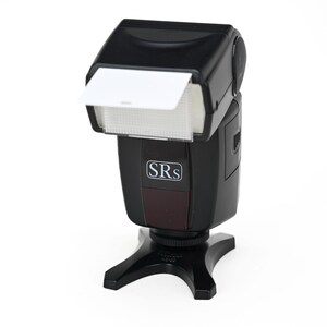 Può includere: Flash per fotocamera nero con diffusore bianco e la scritta "SRs". Il flash è montato su un supporto nero. Il flash è progettato per l'uso con fotocamere e fotografia.