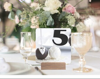 May include: A white and black cake pop with a tuxedo design and a white cake pop with a white bow. The cake pops are on a wooden stand with a white background and the number 5 in black.