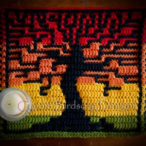 Op de afbeelding: Een gehaakt wandkleed met een boom met een zwarte stam en kleurrijke bladeren in tinten rood, oranje, geel en groen. Het wandkleed heeft franjes aan alle kanten en bevat de tekst "Cynthie Birdsong Designs".