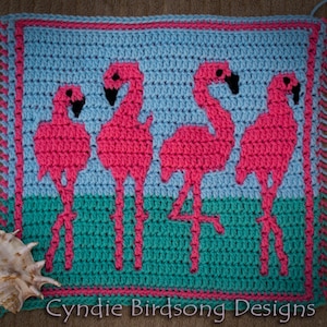 May include: Crocheted square with a blue and green background featuring four pink flamingos. The square has a pink border and fringe on all sides. The text "Cynie Birdsong Designs" is at the bottom of the square.