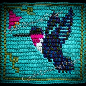May include: Crocheted square featuring a hummingbird in flight, with a pink flower in its beak. The hummingbird is made with blue, purple, green, and white yarn. The background is turquoise, with a green border. The text "Cynide Birdsong Designs" is visible in the image.