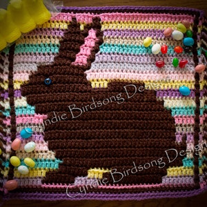 May include: A crocheted Easter bunny blanket with a brown bunny silhouette and colorful stripes. The blanket has fringe on the edges and is decorated with jelly beans.