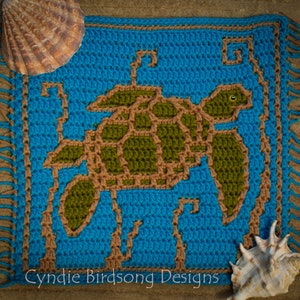 Op de afbeelding: Een gehaakt vierkant met een bruin en groen zeeschildpadontwerp op een blauwe achtergrond. Het vierkant heeft een bruine franje rond de randen. De afbeelding bevat de tekst "Cynie Birdsong Designs".