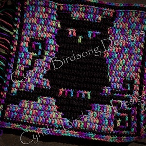 Könnte beinhalten: Ein farbenfrohes Häkelquadrat mit schwarzer Mitte und Fransen an den Rändern. Das Quadrat zeigt den Text "Cynthie Birdsong Designs" zweimal wiederholt.