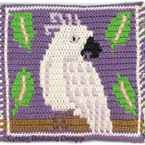 May include: A crocheted square featuring a white cockatoo perched on a brown branch. The cockatoo is surrounded by green leaves with pink accents on a purple background. The square is bordered with a white and pink crocheted trim. The text "Cynie Birdsong Designs" is at the bottom of the square.