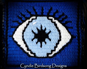 May include: A blue crocheted square with a white and blue eye design. The eye has a black pupil and a white iris. The text "Cynide Birdsong Designs" is at the bottom of the square.