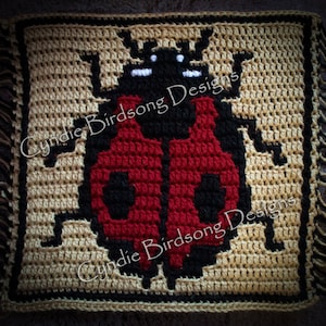 以下が含まれることがあります： 白いつぶつぶのある赤と黒のテントウムシが描かれた、かぎ針編みで作った正方形。正方形は、黒の縁取りのある茶色の枠で囲まれています。正方形には、「CIndie Birdsong Designs」という文字が2回書かれています。