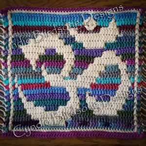 Puede incluir: Un cuadrado tejido a crochet con un diseño geométrico blanco sobre un fondo a rayas de colores. El cuadrado tiene un borde de flecos y el texto "Cynie Birdsong Designs" es visible en la imagen.