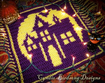 May include: A purple and yellow crocheted Halloween-themed square featuring a haunted house design. The design includes a house silhouette with windows and a bat, surrounded by a yellow border. The text "Cyndie Birdsong Designs" is at the bottom.