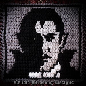May include: Crocheted portrait of a man with a black and white design. The man has a serious expression and is wearing a white collar. The crochet piece is framed with a fringe border.