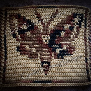 Op de afbeelding: Gehaakt vierkant met een bruin, zwart en beige adelaarontwerp. Het vierkant heeft een franje rand en de tekst "Cynthia Birdsong Designs" is zichtbaar in de rechterbovenhoek.