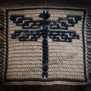 May include: A crocheted square with a black dragonfly design in the center. The square has a black border and fringe around the edges. The text "Cynthie Birdsong Designs" is visible in the image.