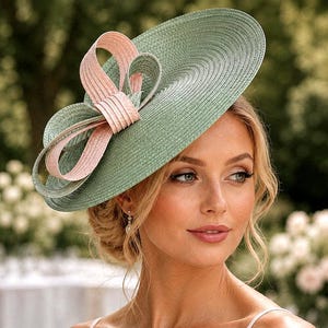May include: A wide-brimmed, light green hat with a large, decorative bow in shades of pink. The hat has a textured surface and is designed for formal events. The bow adds a touch of elegance to the overall design.