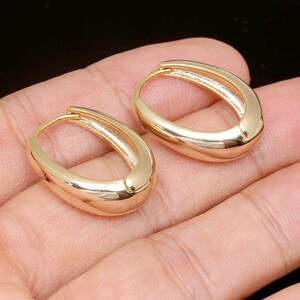 May include: A pair of gold hoop earrings with a smooth, oval shape.