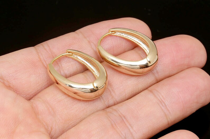 May include: A pair of gold hoop earrings with a smooth, oval shape.