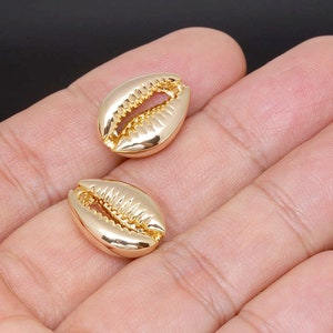 May include: Two gold-coloured cowrie shell charms. The shells are smooth and have a detailed texture.