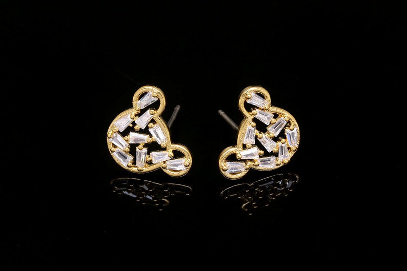 K&ouml;nnte beinhalten: Ein Paar goldfarbene Ohrringe mit einem Mickey-Maus-Silhouetten-Design. Die Ohrringe sind mit klaren Zirkonia-Steinen verziert.