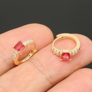 May include: A pair of gold hoop earrings with a red square gemstone and clear cubic zirconia accents.