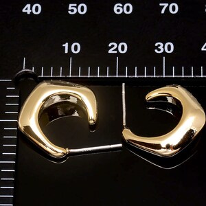Puede incluir: Un par de pendientes de aro dorados con un dise&ntilde;o &uacute;nico, ligeramente angular. Los pendientes miden aproximadamente 2 cm de di&aacute;metro.