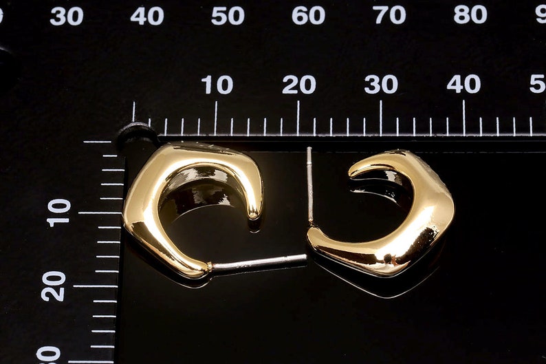 Puede incluir: Un par de pendientes de aro dorados con un dise&ntilde;o &uacute;nico, ligeramente angular. Los pendientes miden aproximadamente 2 cm de di&aacute;metro.