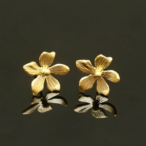 Puede incluir: Un par de pendientes de botón de oro en forma de flor. Los pendientes están hechos de un metal brillante y tienen un diseño delicado y femenino.