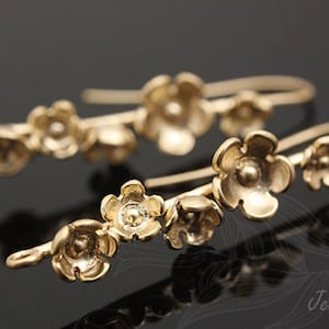 May include: A pair of gold-toned earrings with a delicate floral design. Each earring features a series of small, flower-shaped charms connected by a thin wire.