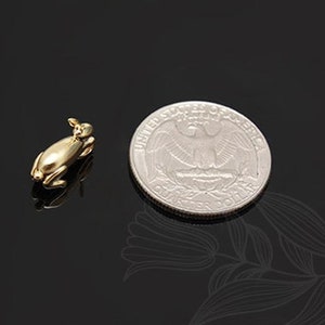 Puede incluir: Una peque&ntilde;a figurita de conejo de color dorado, tumbada, junto a una moneda de 25 centavos de d&oacute;lar estadounidense para comparar el tama&ntilde;o.