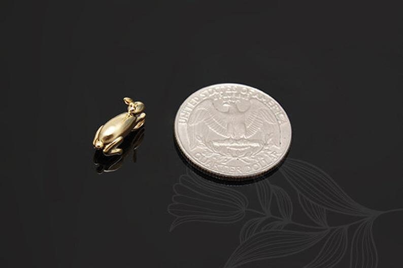 Puede incluir: Una peque&ntilde;a figurita de conejo de color dorado, tumbada, junto a una moneda de 25 centavos de d&oacute;lar estadounidense para comparar el tama&ntilde;o.