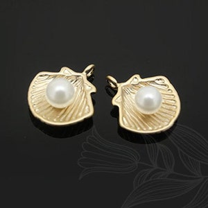 May include: Two gold-tone shell-shaped charms with a pearl in the center. The charms have a detailed design and are perfect for jewelry making.