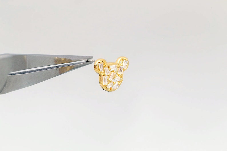 K&ouml;nnte beinhalten: Goldfarbener Ohrring mit einem B&auml;renmotiv, besetzt mit klaren Baguette-Steinen.