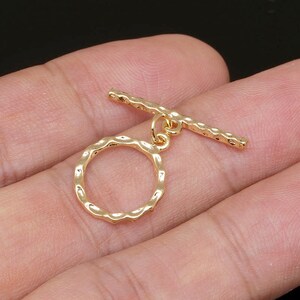 Puede incluir: Cierre de palanca de metal dorado con un anillo redondo texturizado y una barra recta. El cierre está diseñado para la fabricación de joyas.