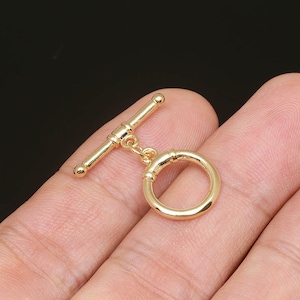 Puede incluir: Cierre de palanca de metal dorado con un anillo redondo. El cierre está diseñado para la elaboración de joyas y es una opción popular para collares y pulseras.