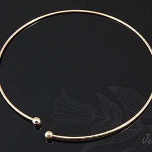 May include: A gold-toned choker necklace with a simple, minimalist design. The necklace is made of a thin, round wire and has two small, round beads at the ends.