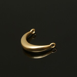 May include: A gold-colored metal crescent-shaped pendant with two small loops at the ends.